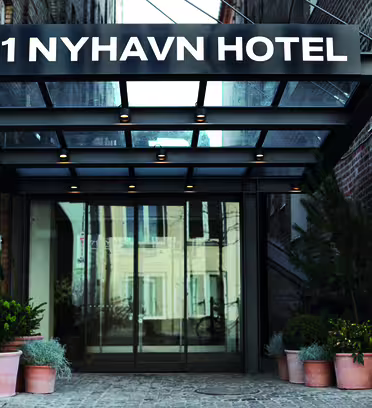 Indgang til 71 Nyhavn Hotel med glasdøre under sort markise. Facaden er udført i røde mursten, og flere potteplanter pryder indgangspartiet.